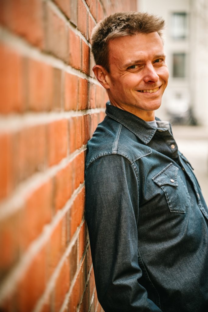 Finanzcoach Robert Mayer an Wand lehnend.