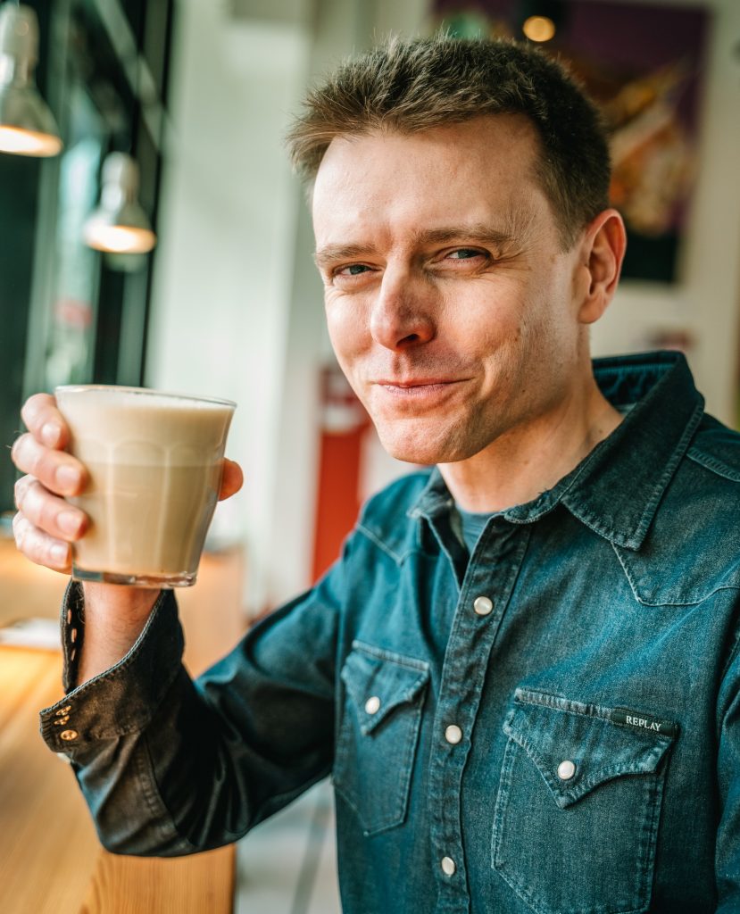 Robert Mayer mit Chai Latte in der Hand freut sich auf Deine Nachricht.